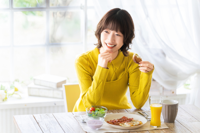 黄色い服を着て朝ごはんをお食べる女性の写真