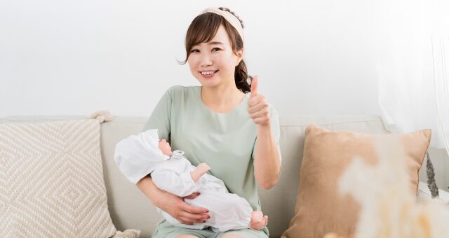 赤ちゃんを抱っこしてOKサインする女性