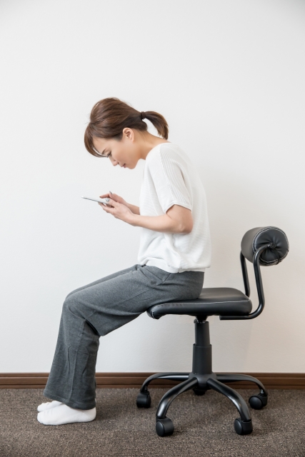 スマホを見て猫背の座っている女性